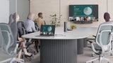 A photograph of a meeting room. There is a large table in the middle of the room where four people are seated facing a wall-mounted TV screen and Logitech Rally Bar. The TV screen shows an active meeting being run from a laptop on the table, connected via Logitech Extend. There are also a Logitech Sight and meeting room touch controller on the table.