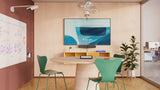A photo of a meeting room with a TV on one wall and a whiteboard on the left wall. Underneath the TV is the Logitech Rally Bar Huddle. Overhanging the whiteboard is the Logitech Scribe. In the middle of the room is a round table surrounded by three green chairs.